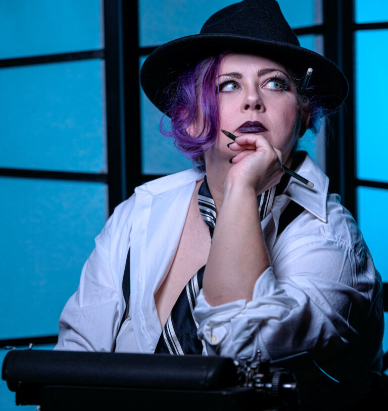 Image of Rebecca Rose Vassy against a black and blue background, wearing a white shirt and black and white tie and a black hat, seated at a typewriter, holding a pencil and staring off into the distance.